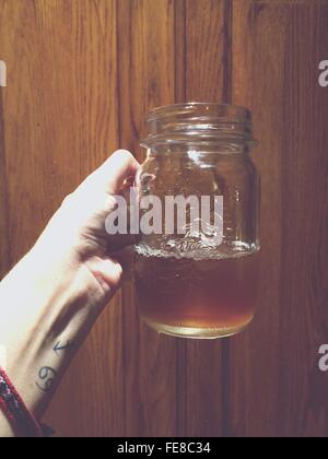 Close-Up Of Hand Holding Glass Jar Of Pale Ale Against Wooden Background