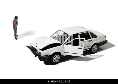 Toy Man Looking at Wrecked Automobile on a White Background Stock Photo