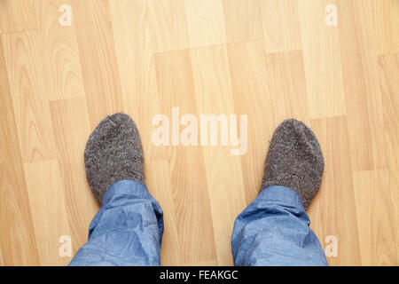 Male feet in blue pants and gray woolen socks stand on wooden parquet Stock Photo