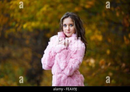 Portrait of beautiful girl in a pink fur coat on a background of yellow leaves Stock Photo