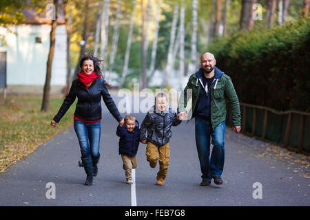 Happy family running on the road in a park at autumn time Stock Photo