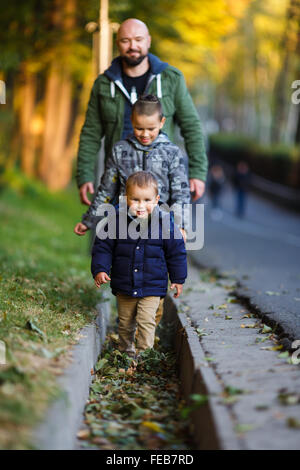 Father with two sons walking in a park at autumn time Stock Photo