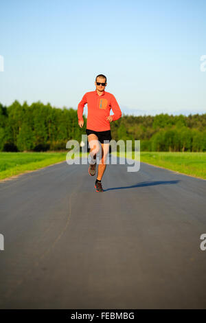 Man runner running on country road, training inspiration and motivation in summer sunset. Young athlete male training and doing Stock Photo