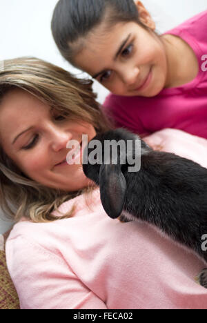 Mother and daughter playing with pet rabbit at home Stock Photo