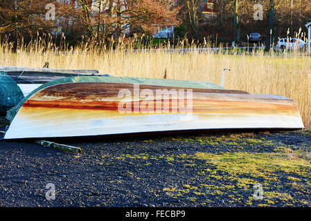 One plastic boat turned upside down on land during winter. The keel is very discolored after years of use. Reeds in background. Stock Photo