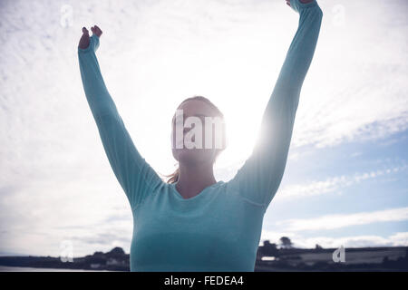 young brunette woman raising her arms on the beach in a white dress ...
