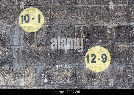 Black numbers in a yellow circle painted on dark brickwork wall in the outdoors in Europe Stock Photo
