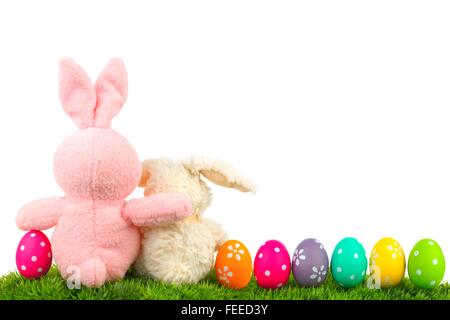 Hugging Easter bunnies on grass with colorful egg border over white, behind view Stock Photo