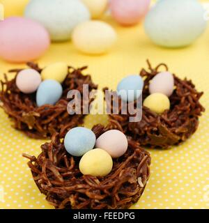 Springtime chocolate nests filled with Easter eggs on a yellow background Stock Photo
