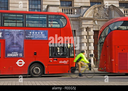 Cyclist wearing high visibility jacket passing red double decker buses on Whitehall in London. London buses are operated by Transport for London. Stock Photo