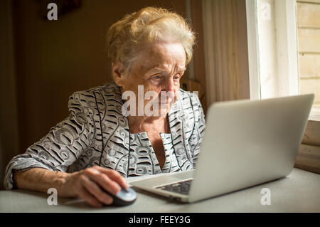 Elderly woman working on laptop at home sitting at the table.