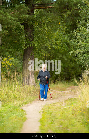 An elderly woman on a walk in the Park practicing Nordic walking. Stock Photo