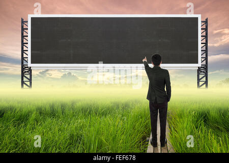 business man standing on wood bridge between rice field and pointing with empty large sign blank for text Stock Photo