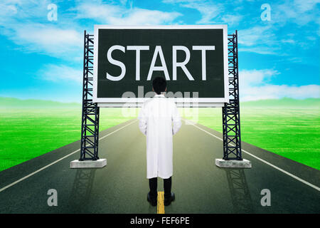 male doctor standing on road and looking with large sign of start Stock Photo