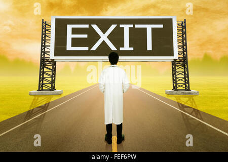 male doctor standing on road and looking with large sign of exit at sunset Stock Photo