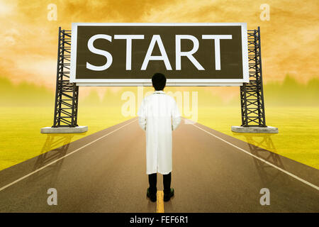 male doctor standing on road and looking with large sign of start at sunset Stock Photo