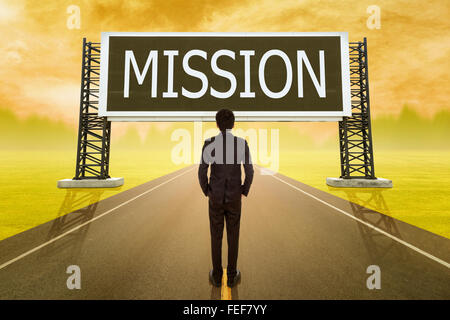 businessman standing on road and looking with large sign of mission at sunset Stock Photo