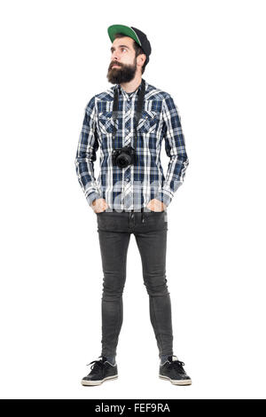 Relaxed hipster wearing black dslr camera over neck with hands in pockets. Full body length portrait isolated over white Stock Photo