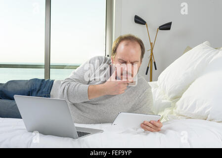 man lying in bed thinking working on tablet and laptop computer Stock Photo