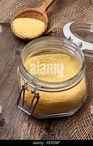 couscous in a glass jar on a wooden background, wooden spoon with couscous Stock Photo