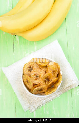 Banana Chips in Bowl over green wooden background, Top View Stock Photo