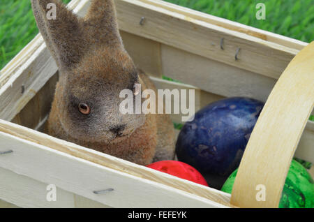 close up of an Easter bunny with Easter eggs, sitting in a basket, outside on green grass, horizontal, full frame Stock Photo