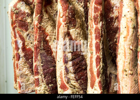 Full frame view of uncut sides of smoked bacon hanging on hooks in a butchery during the aging process Stock Photo