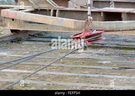 A red metal pulley with wires attached to a railroad undercarriage used in a marina to pull boats in and out of the sea. Stock Photo