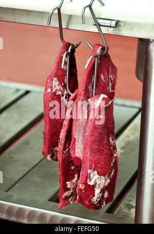 Lean trimmed fillet beef steak hanging in a butchery on meat hooks Stock Photo