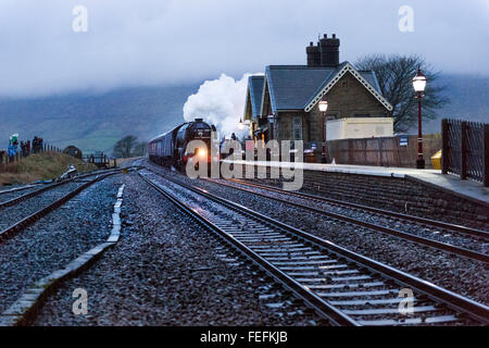 Ribblehead, North Yorkshire, UK. 6th February, 2016. The famous Flying Scotsman steam locomotive runs over the Settle-Carlisle Railway Line past Ribblehead Station, North Yorkshire, late on 6th February 2016. This is the loco's first outing on the Settle-Carlisle since its recent restoration. Stock Photo