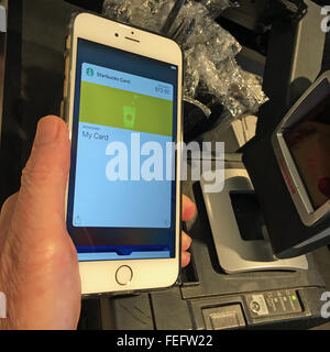 Man pays for coffee using his Starbucks card within the Apple Pay wallet app on his iPhone 6S Plus. Stock Photo