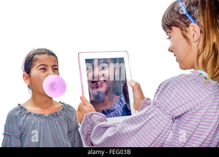 Beautiful little girl taking pictures with tablet of her sister blowing bubbles Stock Photo