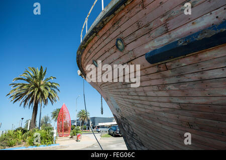 View of bow of an old wooden boat in dry dock. Small port holes can be seen along with palm trees in background. Stock Photo