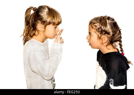 Little girl telling her sister to shut up with her finger on the mouth. A gesture of silence . Closeup-Isolated on white Stock Photo