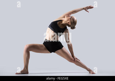 Sporty beautiful young woman practicing yoga, doing high lunge exercise, Reverse Warrior Pose, Viparita Virabhadrasana, working Stock Photo