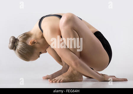 Sporty beautiful young woman practicing yoga, sitting in squat, variation of Garland Pose, Malasana with forward bend Stock Photo