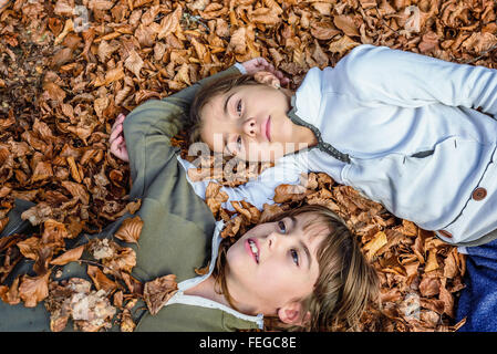 Little girls laying on the bed of leaves in national park Biogradska Gora in autumn, Montenegro Stock Photo