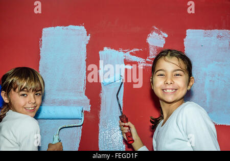 Eight year old twins girls painting the wall at home Stock Photo