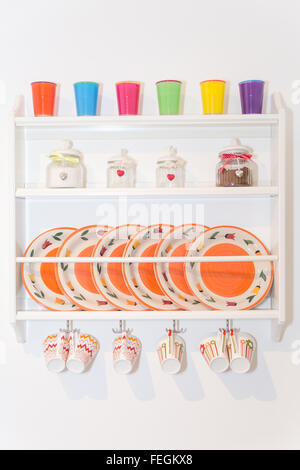 Closeup of Colourful Plates and Dinnerware in a Cupboard on White Wall. Container Seasoning on Shelf. Items Include, Plates, Cof Stock Photo