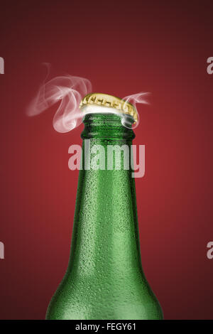 Green cold beer bottle with water drops and golden cap open on red background Stock Photo