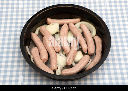 Heck pork Chipolatas sausages in pan with chopped onions Stock Photo