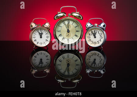 Vintage alarm clocks showing five minutes to twelve, red background Stock Photo