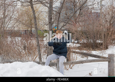 Young boy sitting on a wooden fence preparing to throw a snowball Stock Photo