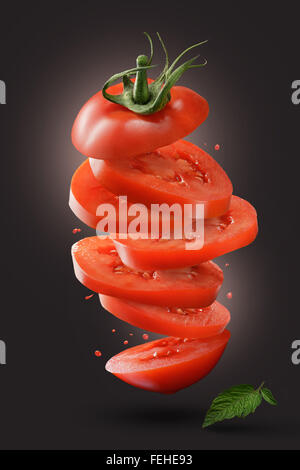 sliced flying tomato with green leaf on dark background Stock Photo