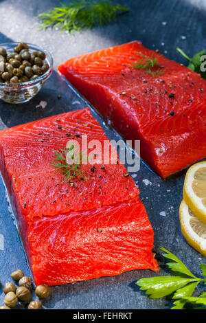 Two pieces of raw wild salmon fish steaks with lemon, capers and herbs, ready to cook Stock Photo