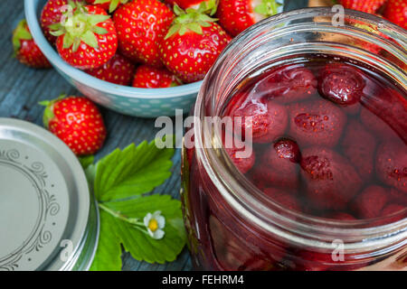 Glass jars with homemade strawberry preserve and fresh strawberries in bowl close up Stock Photo