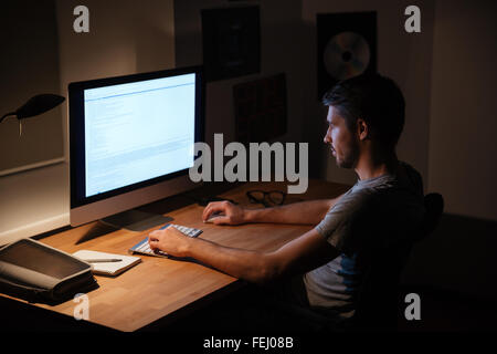 Handsome young man sitting in dark room and using computer Stock Photo