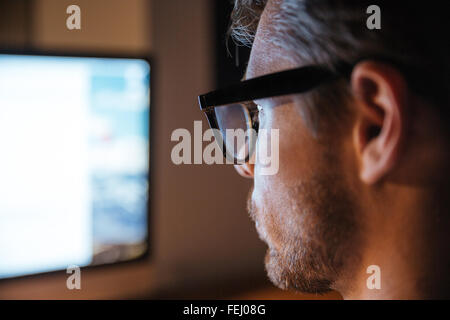 Serious stubbled young man in glasses using computer and looking at screen Stock Photo