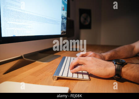 Closeup of keyboard and monitor of computer used by young man on wooden table Stock Photo