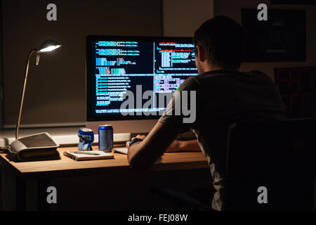Back view of modern programmer sitting and writing code in dark room Stock Photo